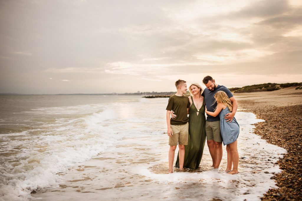 a family of four standing in the waves with their arms around each other by wiltshire family photographer Rachel Jane Photography