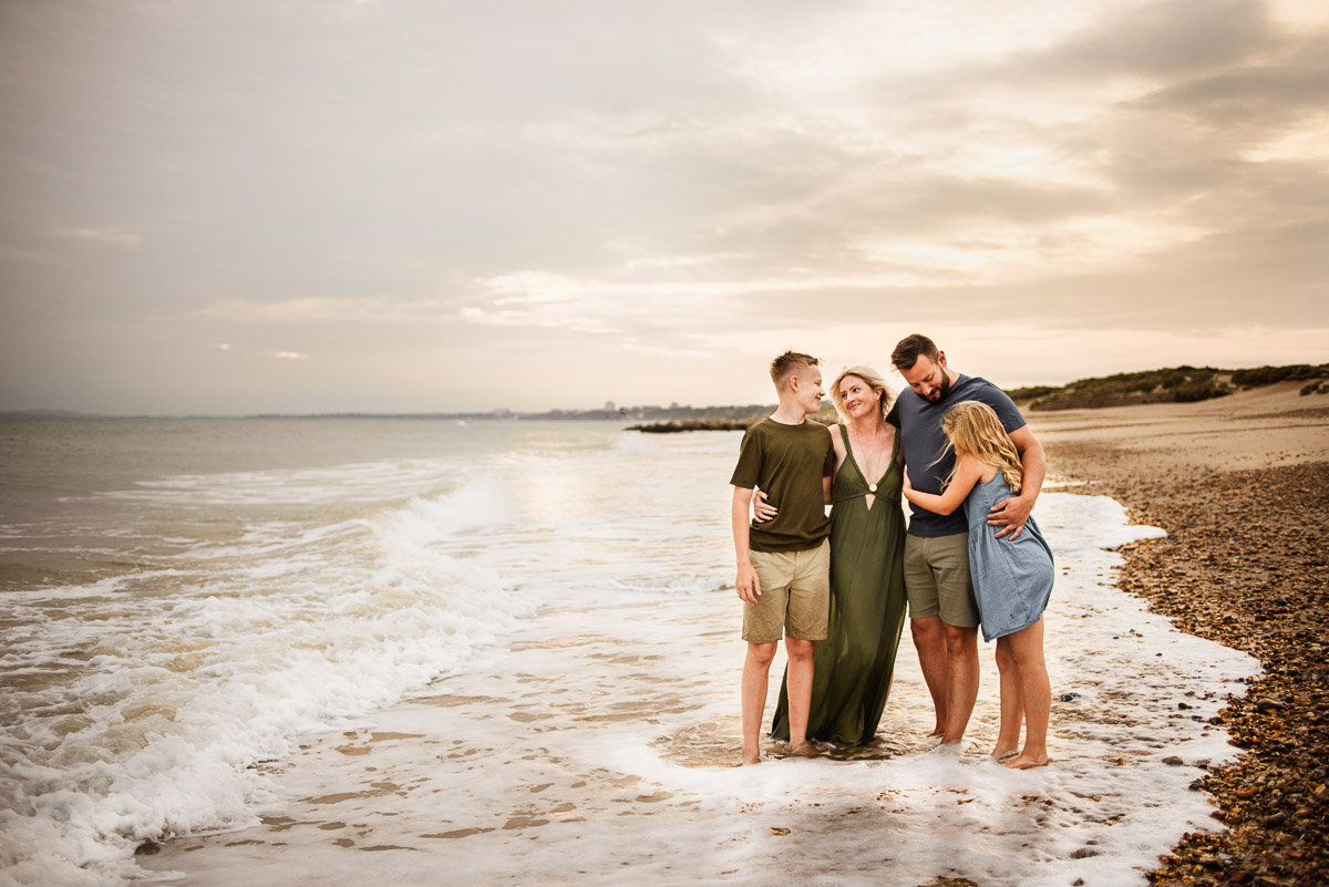a family of four standing in the waves with their arms around each other by wiltshire family photographer Rachel Jane Photography