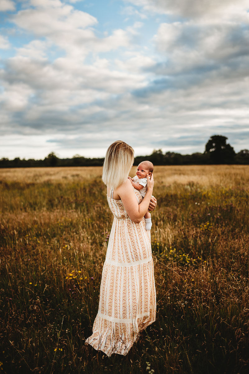 mother holding her baby in a long grass field during sunset