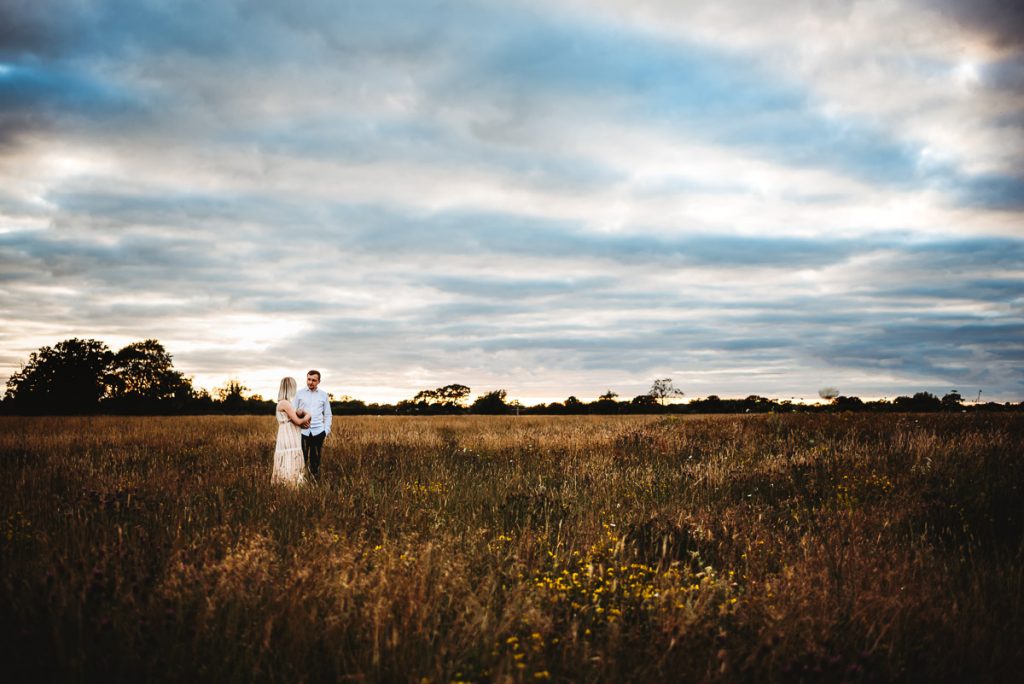 mum and dad holding their newborn baby against a sunset sky