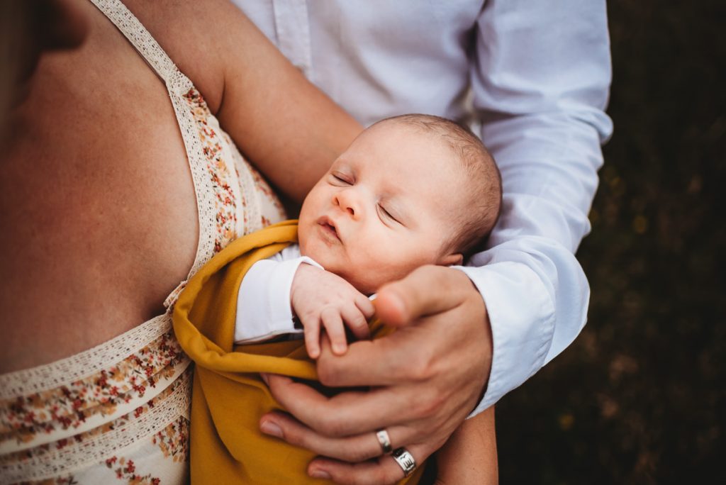 a newborn baby sleeping in his parents arms. Outdoor newborn photography during sunset