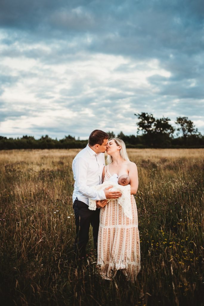 mother standing breastfeeding her newborn baby. Husband is standing close kissing her
