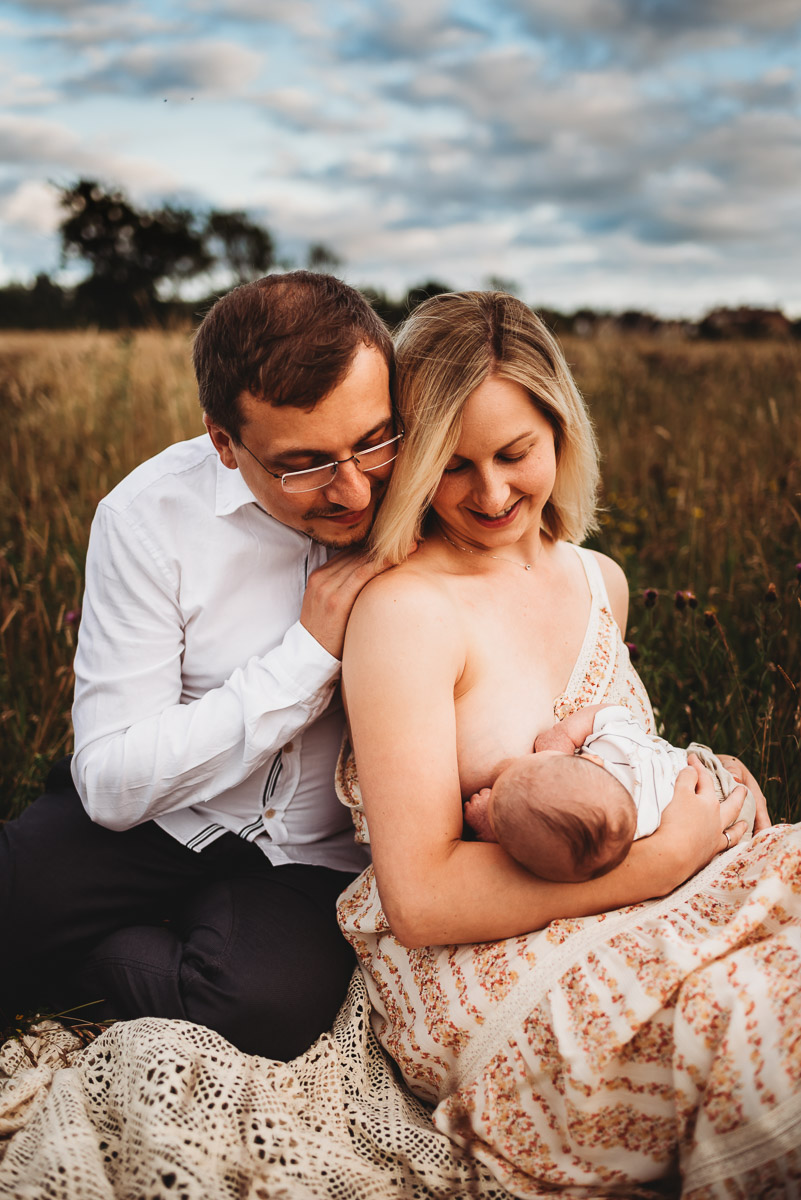 mother and father sitting in a long grass field with their newborn baby