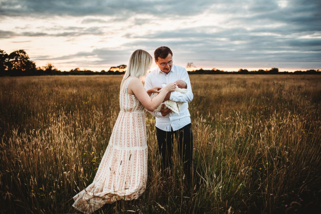 mother and father holding their newborn baby in a field at sunset. Outdoor newborn photography during sunset