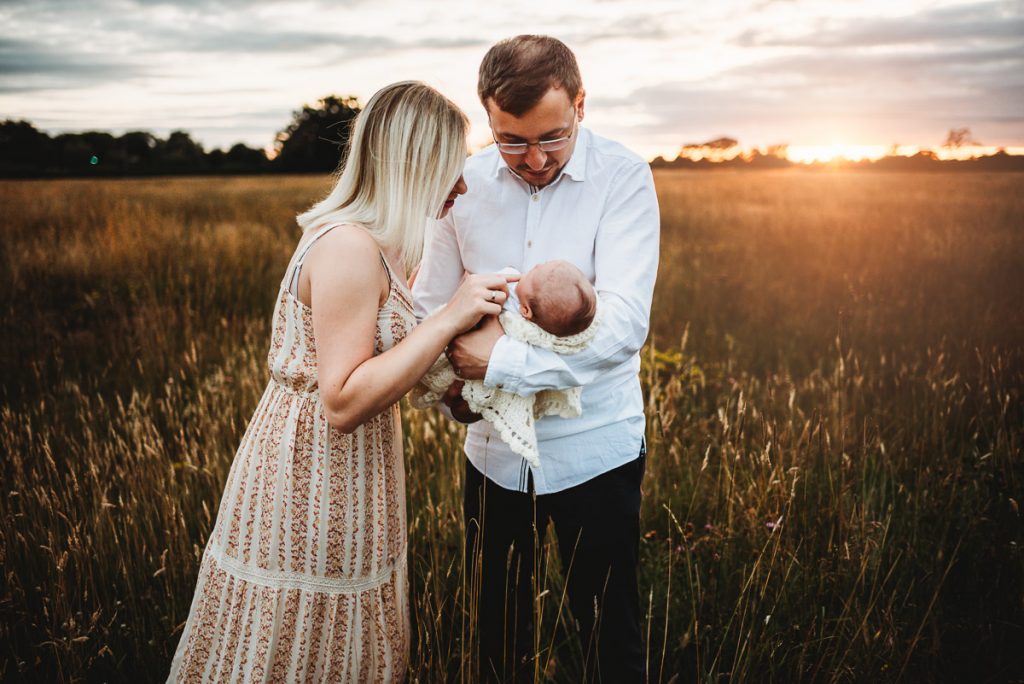 mum and dad with their newborn baby in a field during sunset