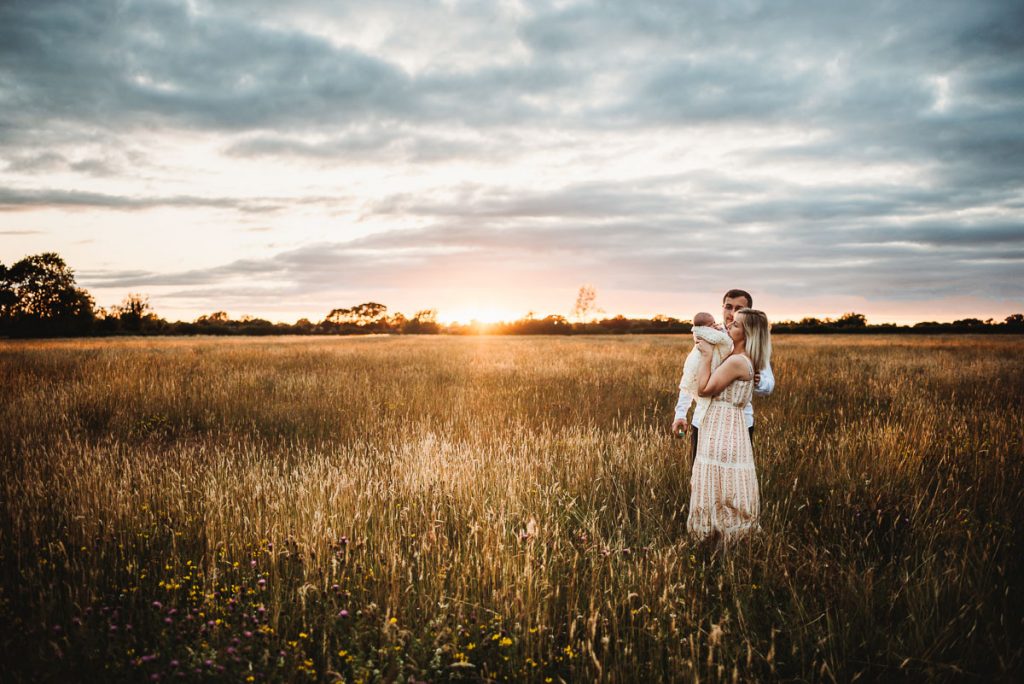 mum and dad with their newborn baby against a dramatic cloudy sky and orange sunset