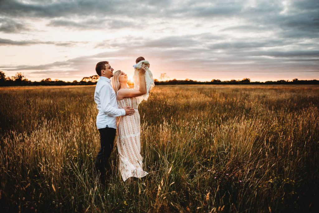 mum and dad holding their newborn baby up to the sky at sunset