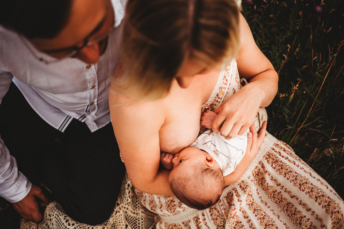 a mother breastfeeding her baby in a field during sunset