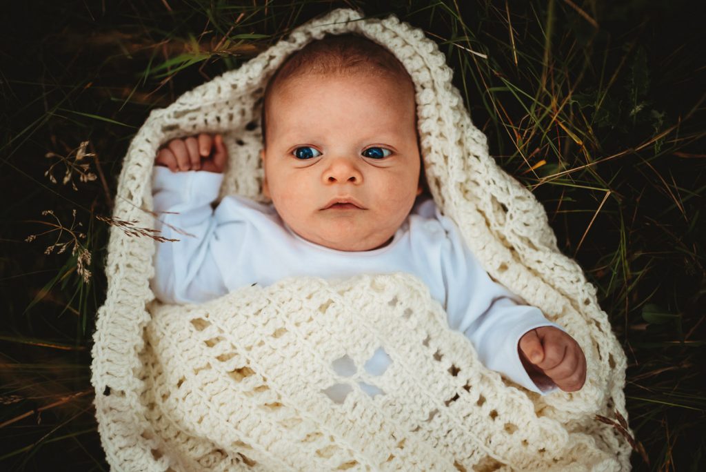 newborn baby wrapped in a blanket lying in long grass