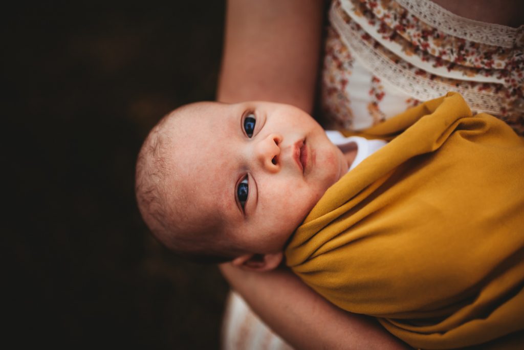 newborn baby wrapped in a mustard coloured blanket. Outdoor newborn photography at sunset