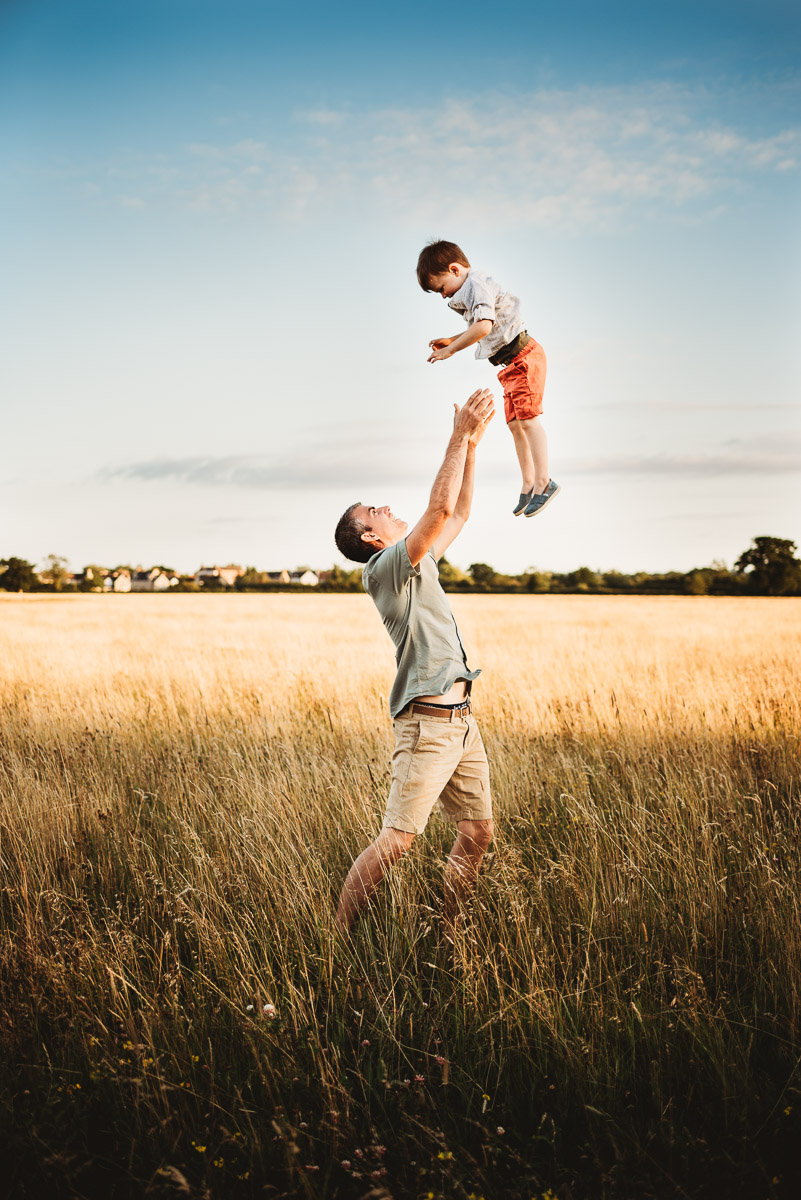 a father throwing his child in the air in a wild meadow field