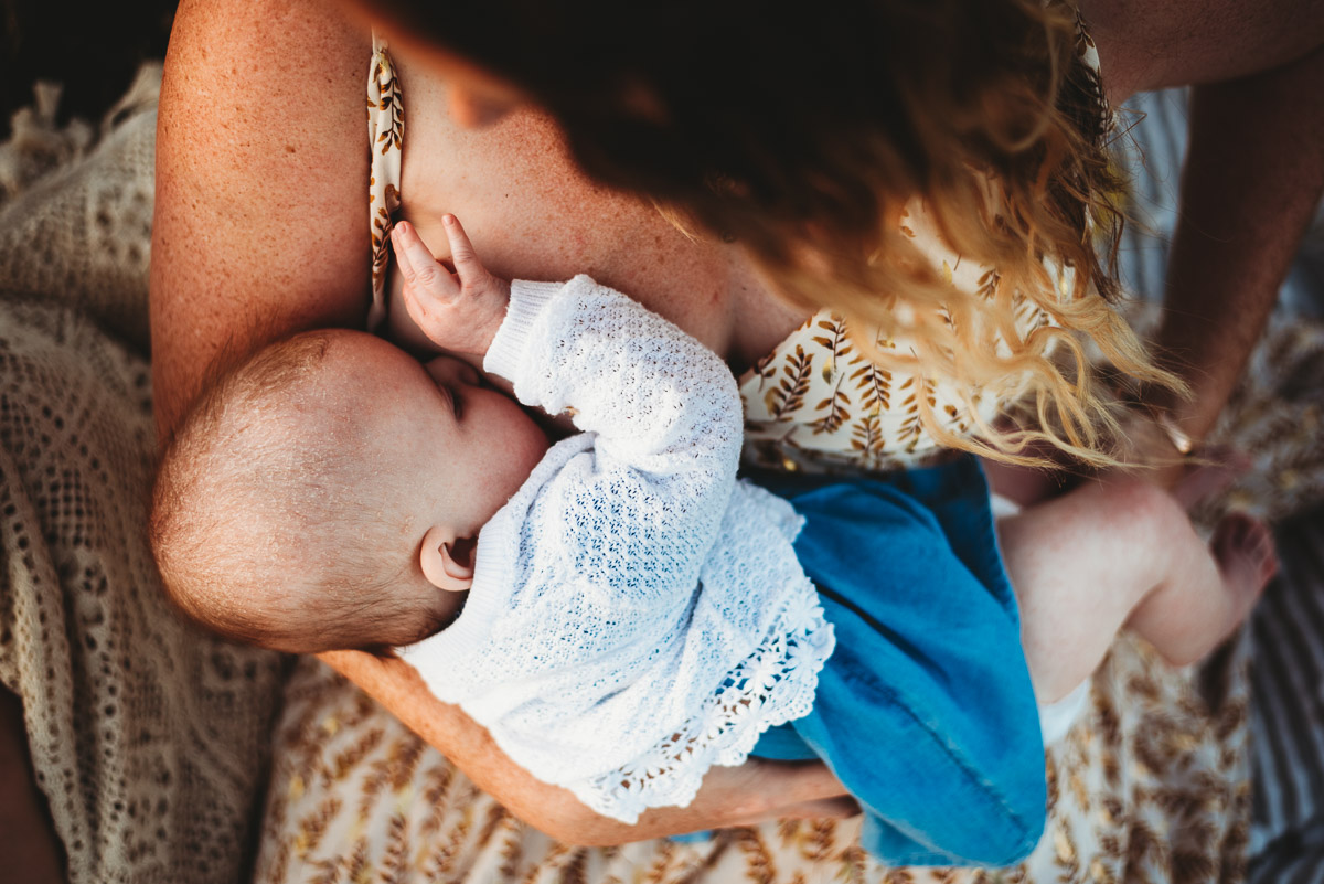 a mother breast-feeding her child in the long grass during sunset