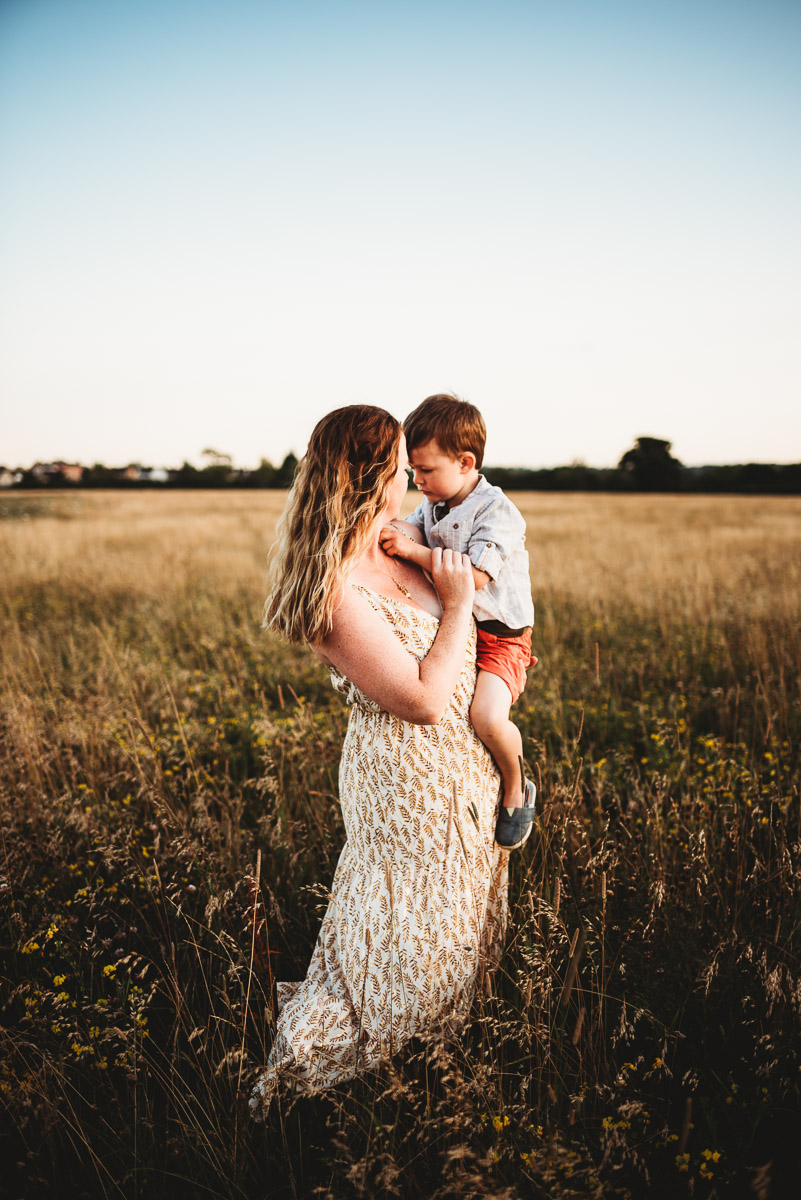 a mother holding her son in a wild meadow field during sunset