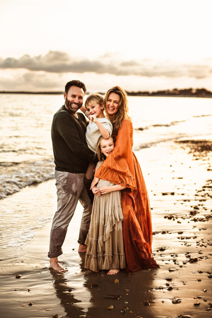 two parents with children on the beach at sunset with the waves behind them by by wiltshire family photographer Rachel Jane Photography