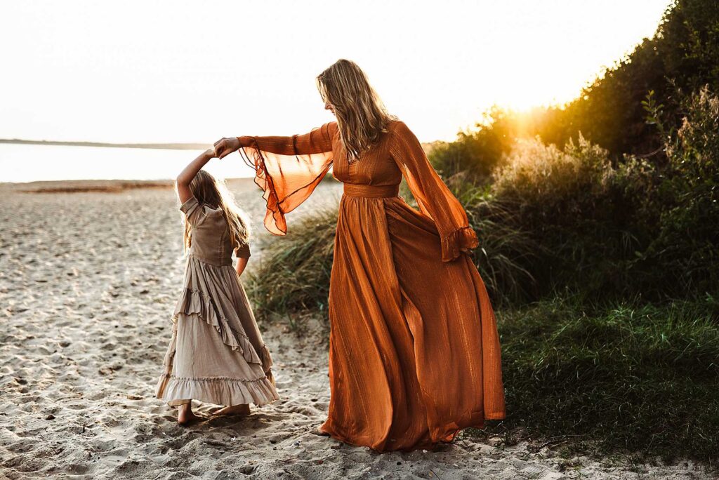 mother and daughter dancing on the beach during sunset