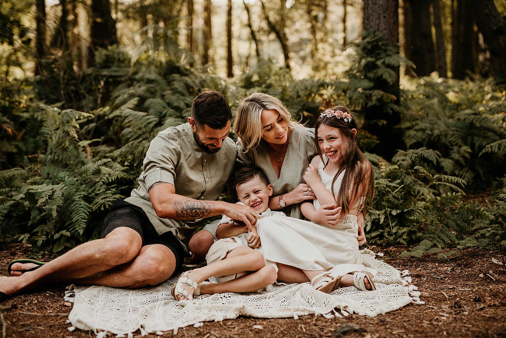 family of four siting on a blanket. Mum and dad are tickling the kids
