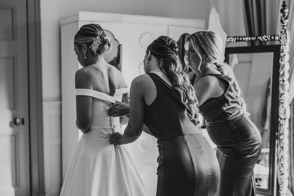 black and white image of bridesmaids helping bride into her dress
