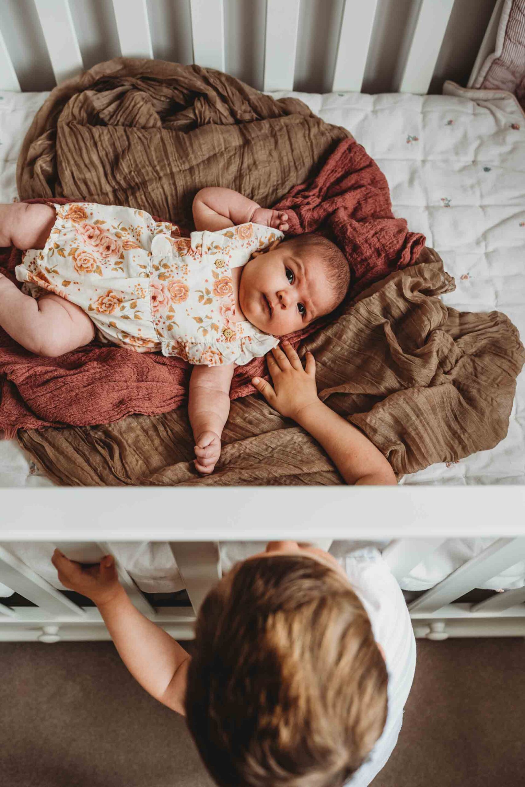 little boy reaching through cot bars to touch his baby sister