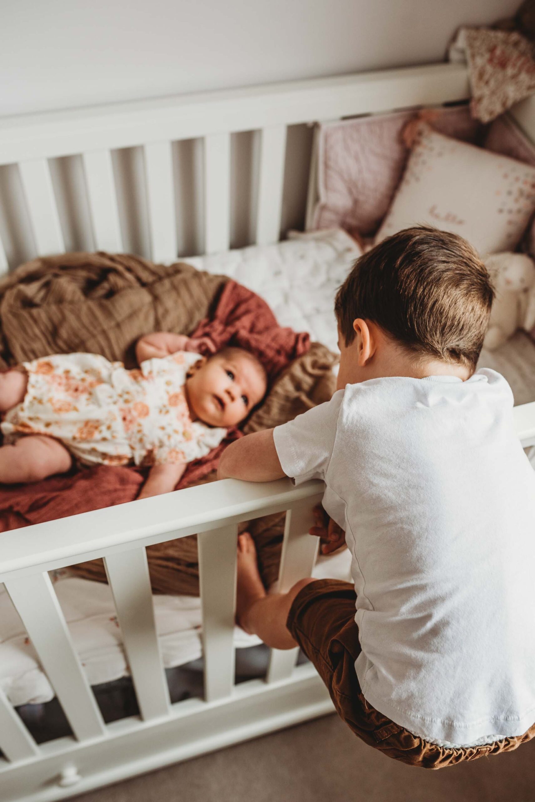 little boy leaning over cot to see his baby sister