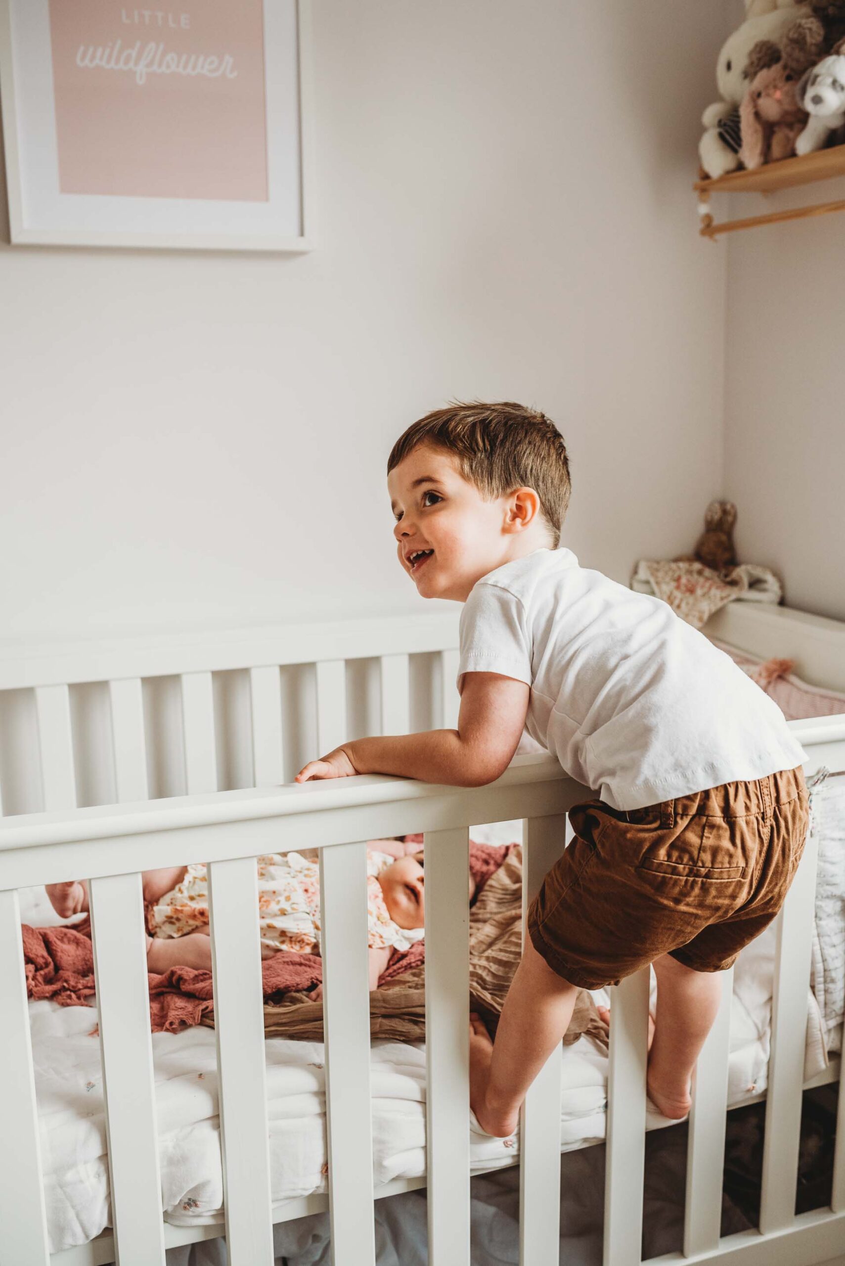 little boy leaning over cot to see his baby sister