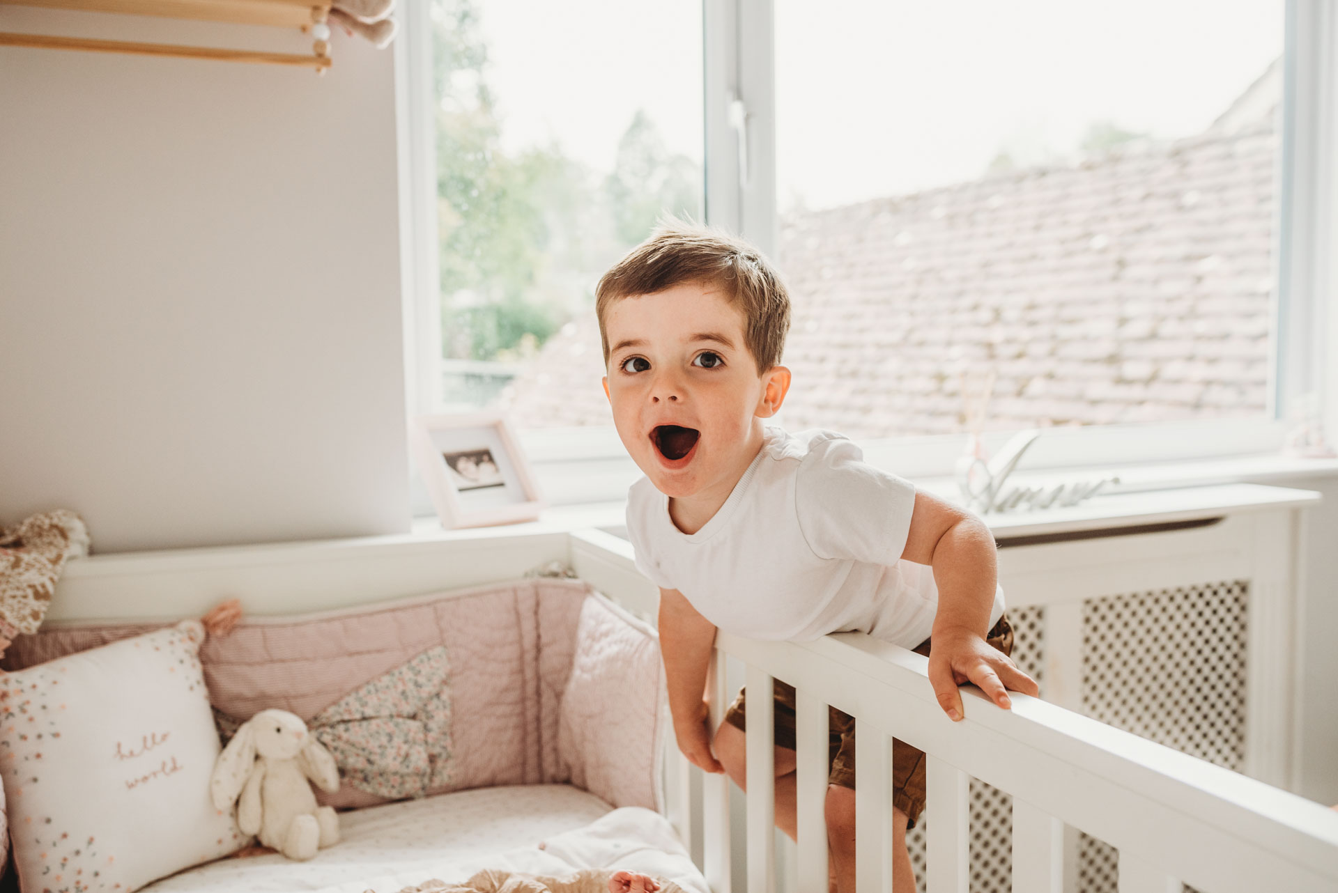 little boy leaning over cot to see his baby sister