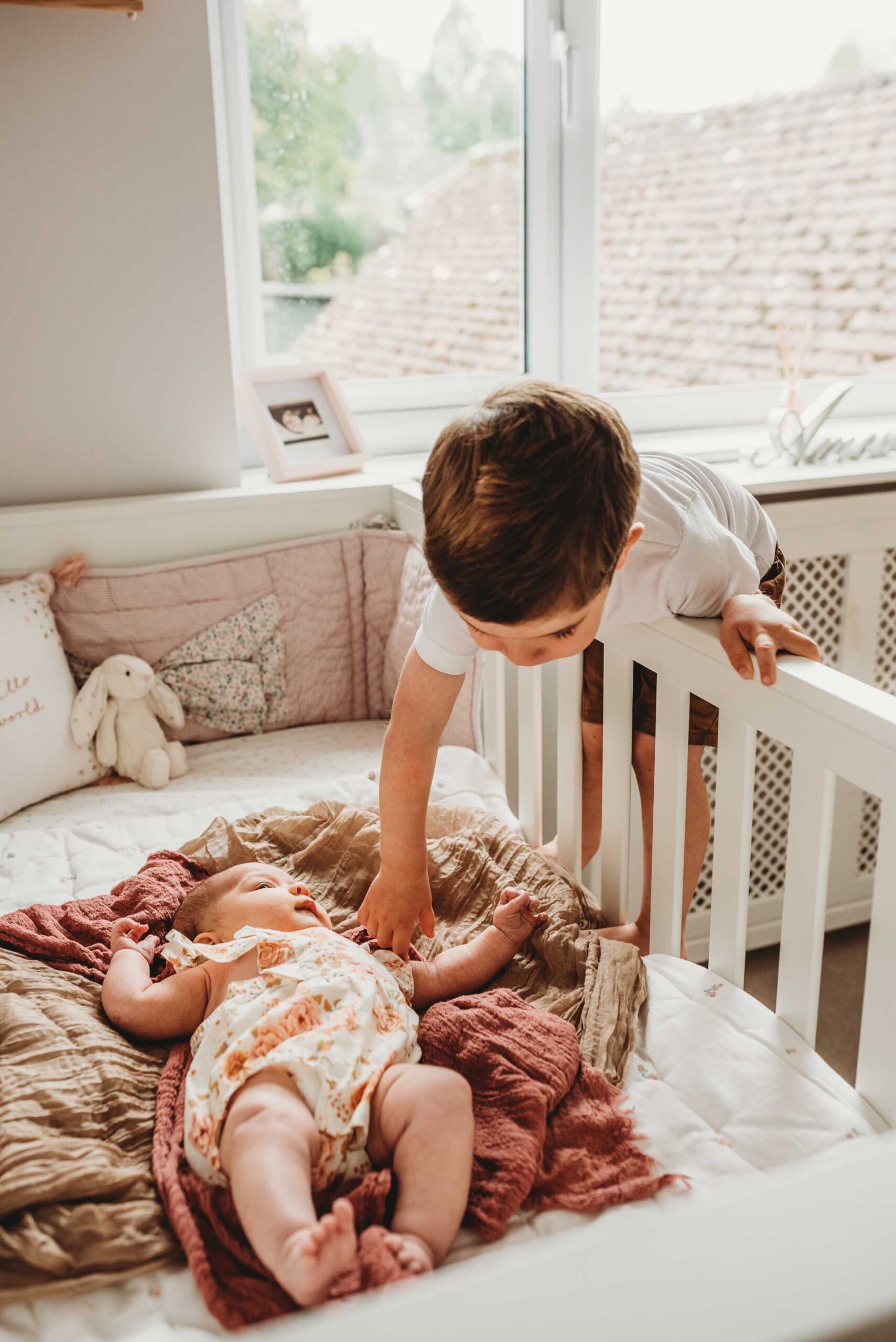 little boy leaning over cot to touch his newborn baby sister