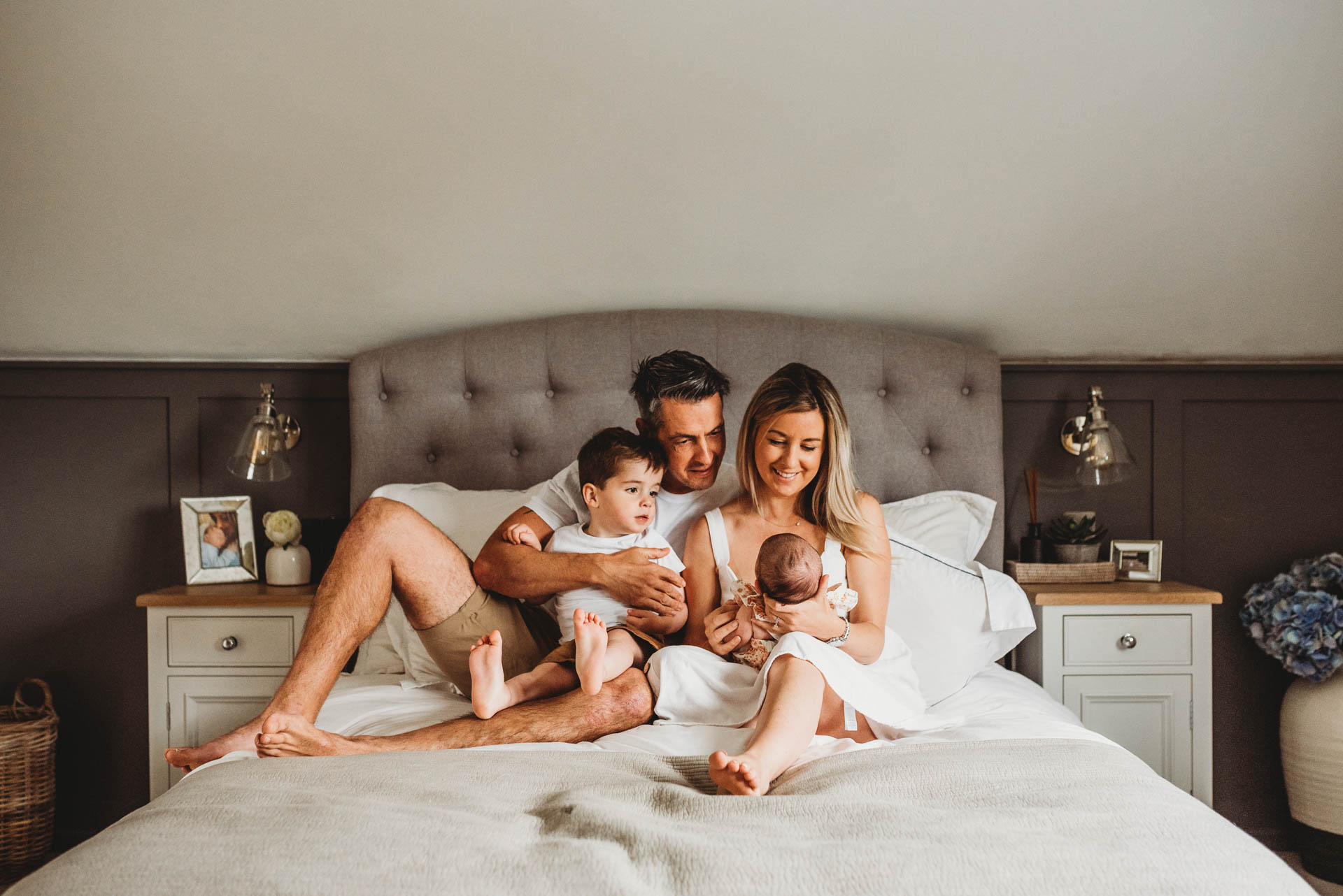 family sitting on bed looking at their newborn baby