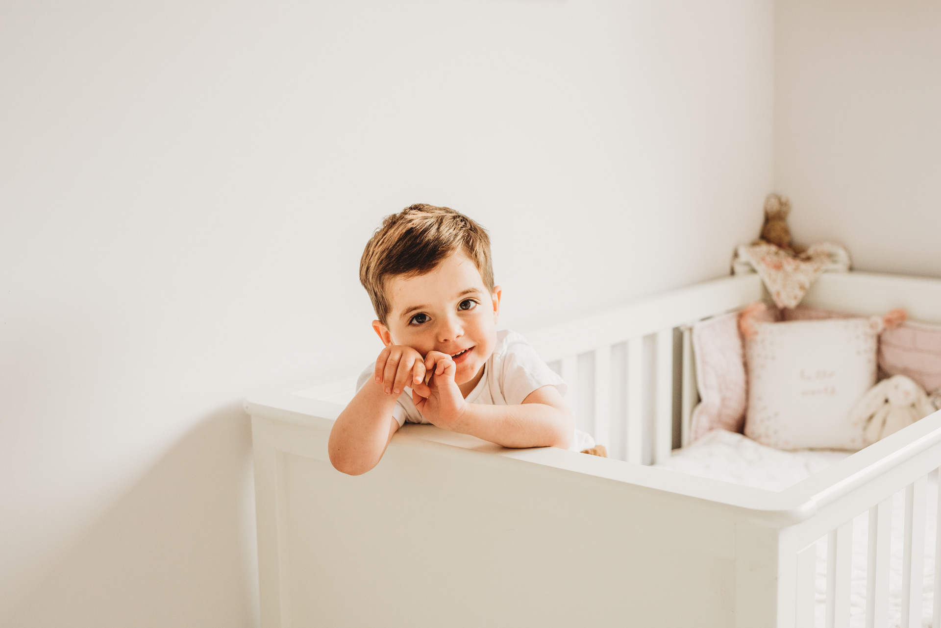 little boy leaning over his baby sisters cot