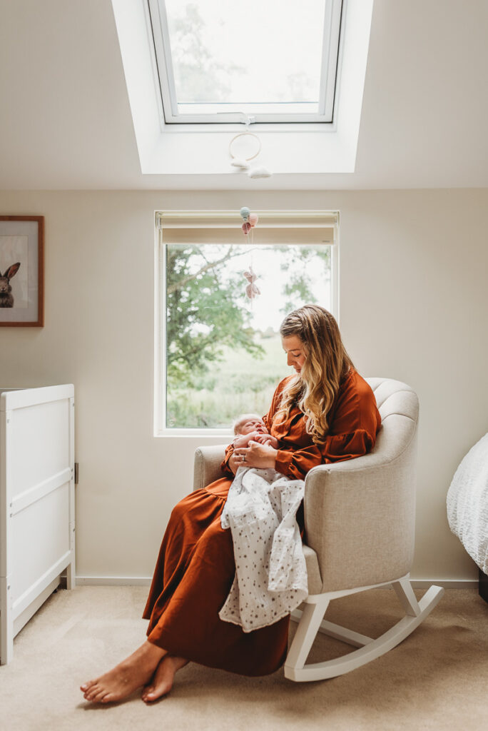 new mother in a cream rocking chair holding her new baby by wiltshire family photographer Rachel Jane Photography