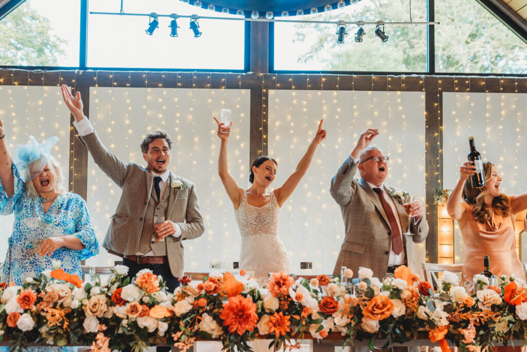 Bride and groom celebrating with arms in the air at their reception by Wedding Photographer in Wiltshire, the Cotswolds, Gloucestershire and beyond.