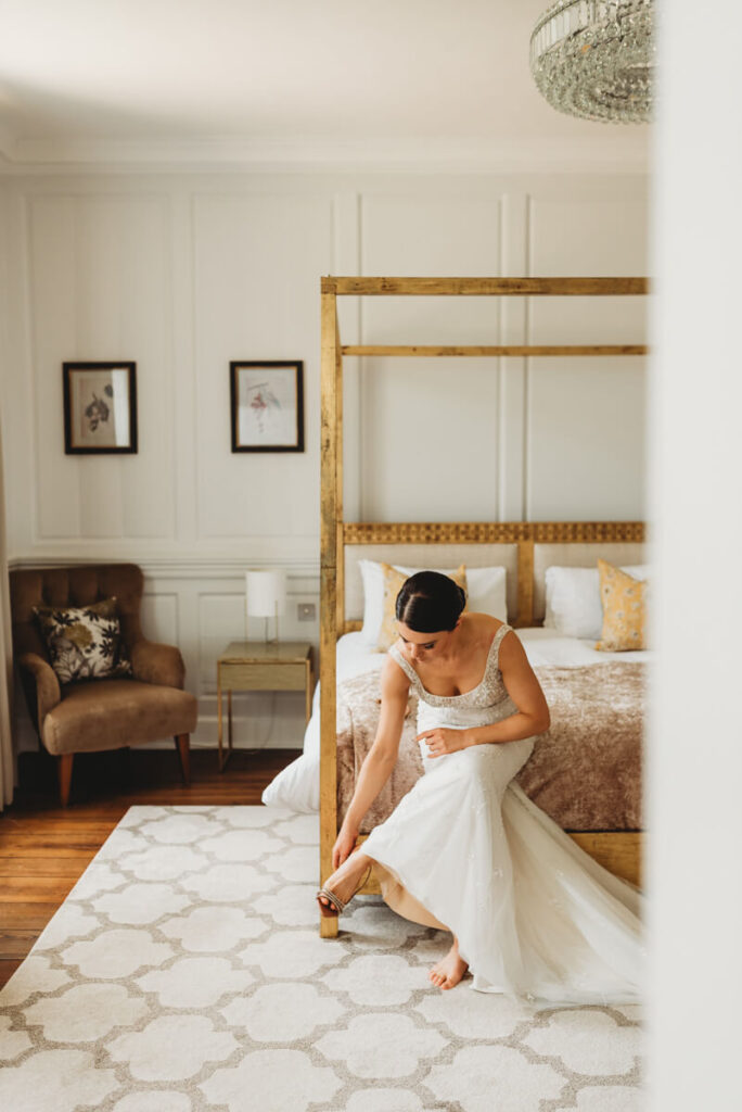 bride sitting on the corner of the bed putting her shoes on at Syrencot house