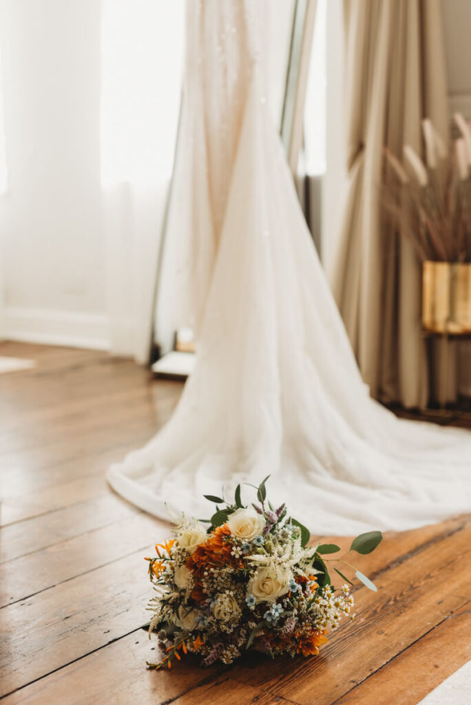 Bridal bouquet sitting next to the brides dress in the bridal suite at Syrencot house