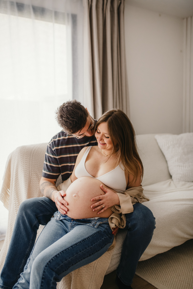 A mum and dad to-be sat together with their hands on her bump during their photoshoot by Swindon maternity photographer Rachel Jane Photography