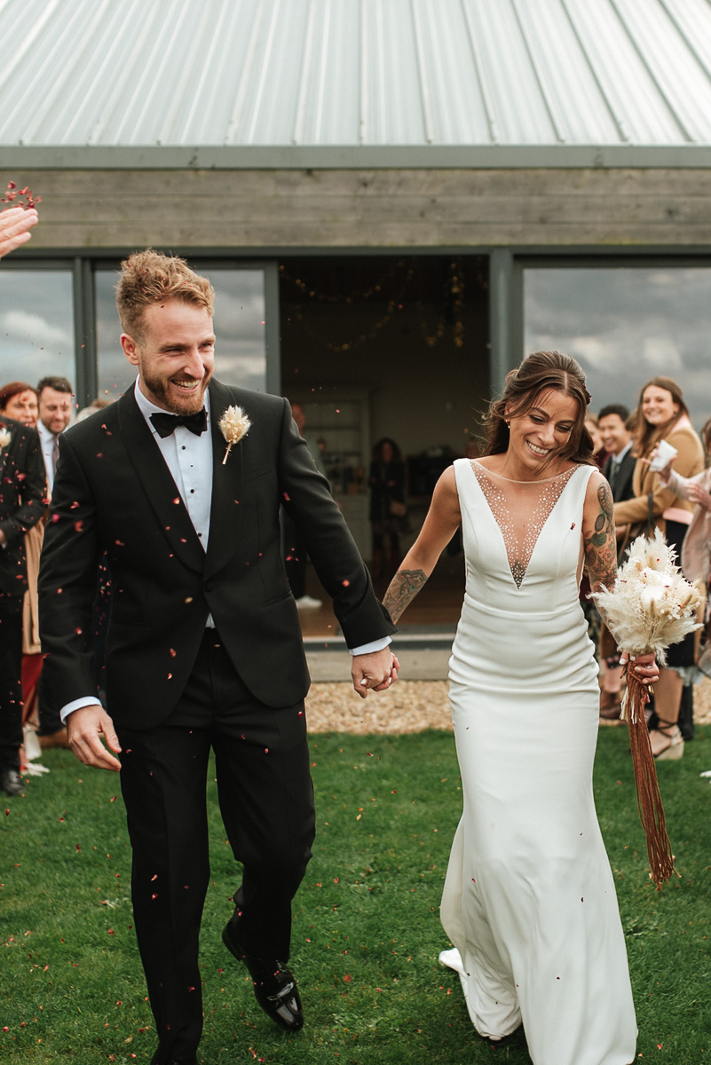 bride and groom walking together as their guests throw confetti over them at chalk barn wedding venue