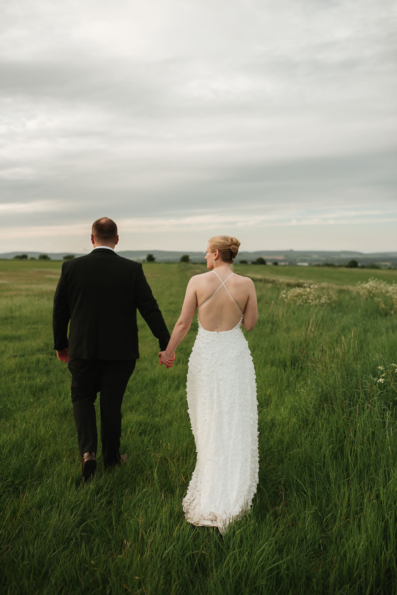 bride and groom walk hand in hand along the rolling hills at chalk barn Wiltshire wedding venue