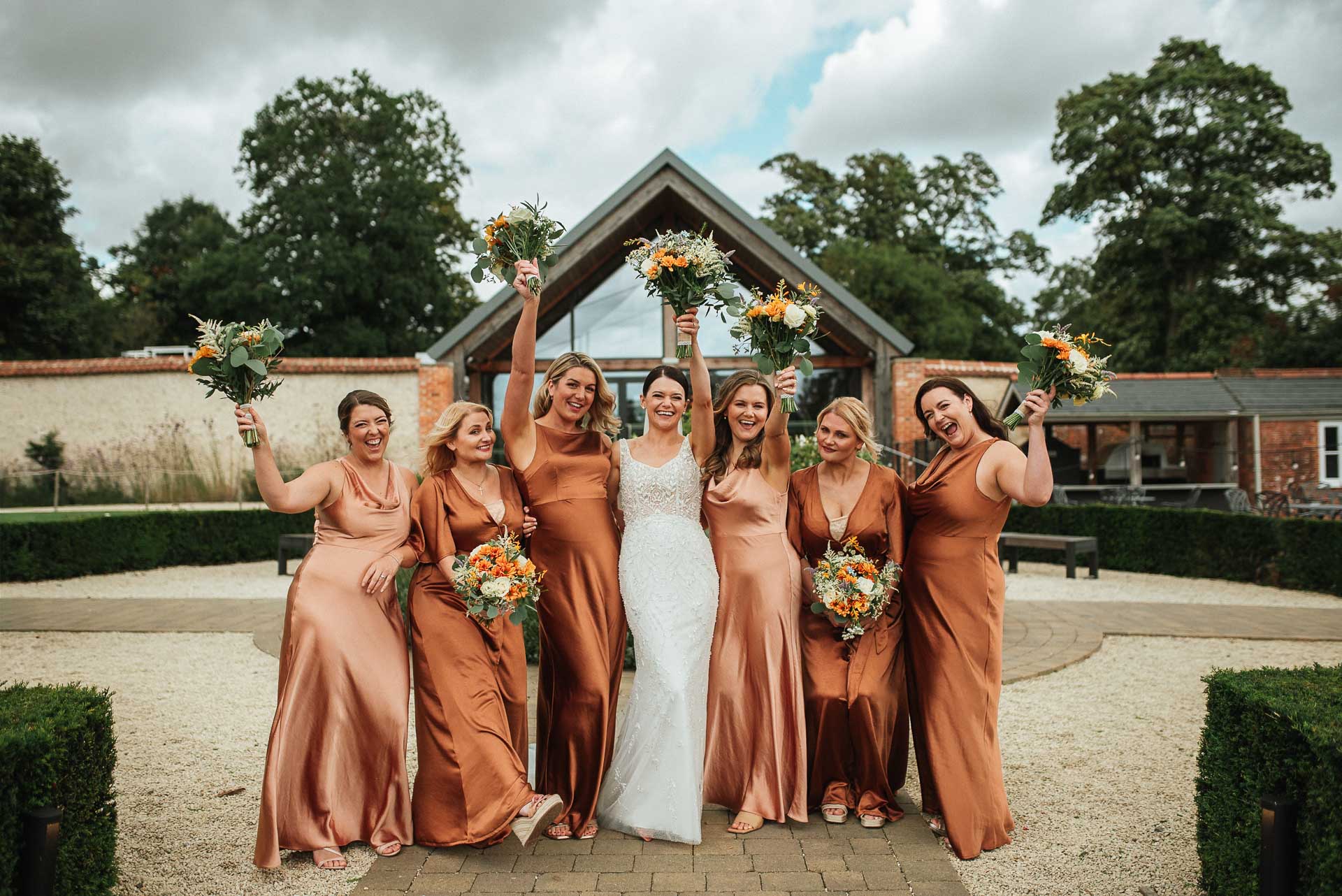 bride and her bridesmaids holding their bouquets in the air outside the orangery at syrencot house