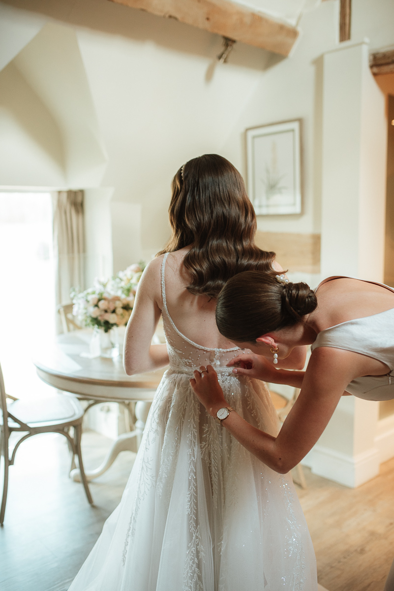 Intimate moment of bridesmaid doing up the brides dress at Lapstone barn