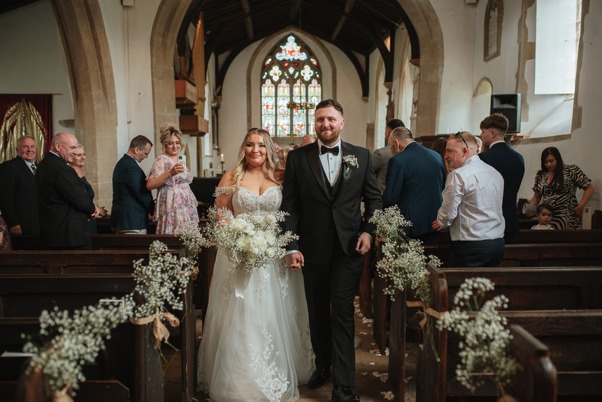 bride and groom leaving the church hand in hand after their ceremony in Wiltshire 