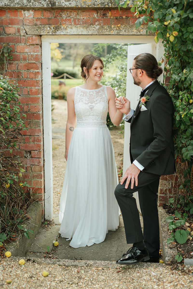 groom taking the hand of his bride as he leads her through the secret garden doorway at syrencot house wedding venue