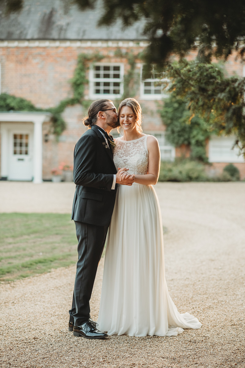 groom kissing his brides cheek as they stand outside during sunset at syrencot house