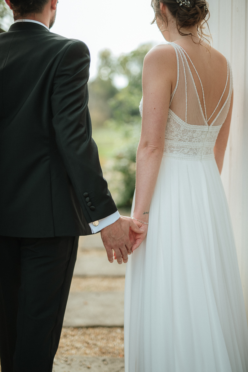bride and groom hand in hand while looking through the doorway at the secret garden at syrencot wedding venue