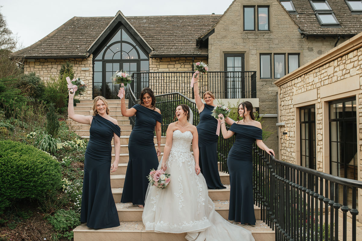 bride and her bridesmaids laughing on the steps at the pear tree purton wedding venue