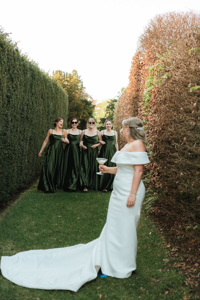 bride standing in the gardens at grittleton house looking back at her bridesmaids walking towards her 