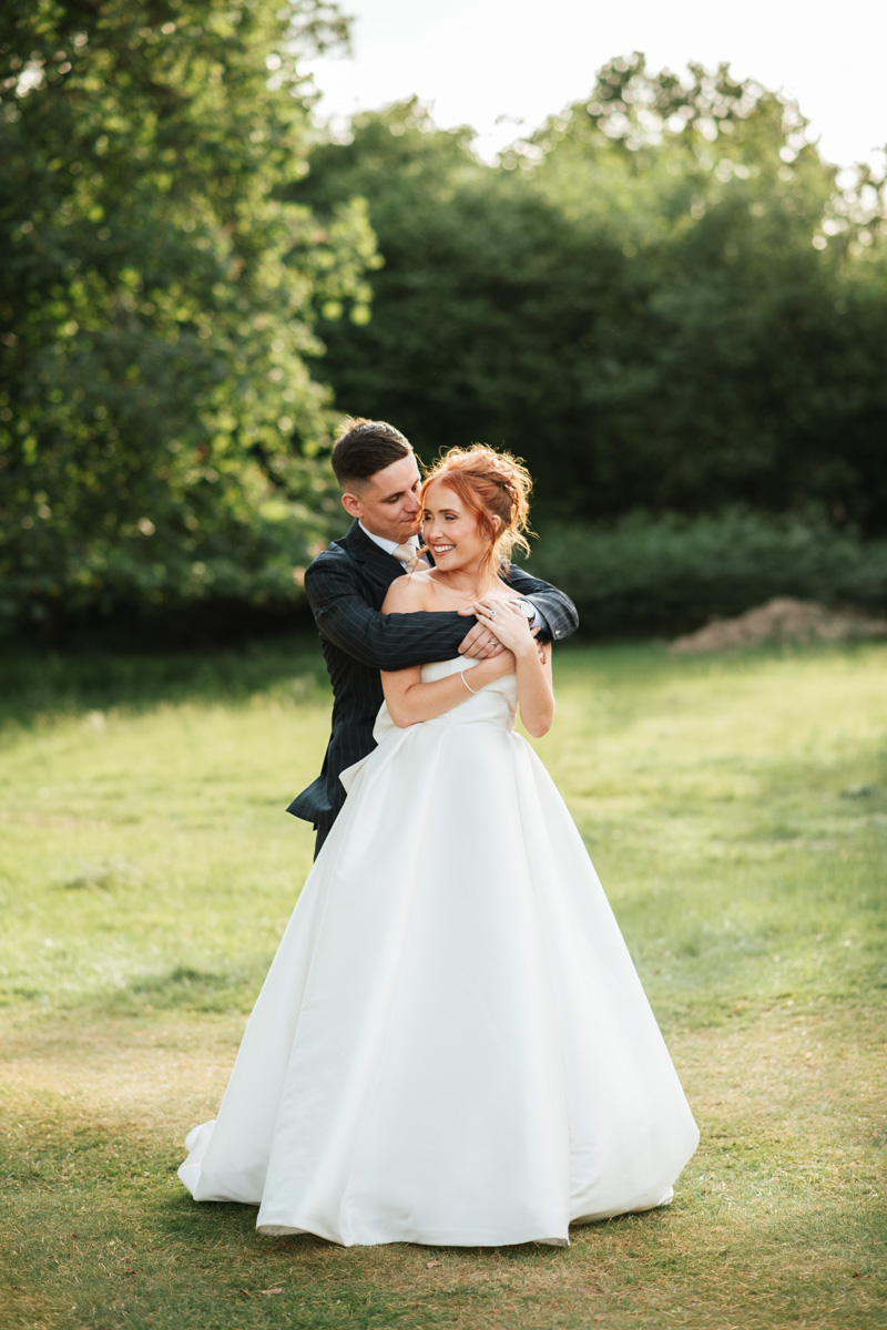 groom embracing his bride from behind as they laugh together at highley manor wedding venue