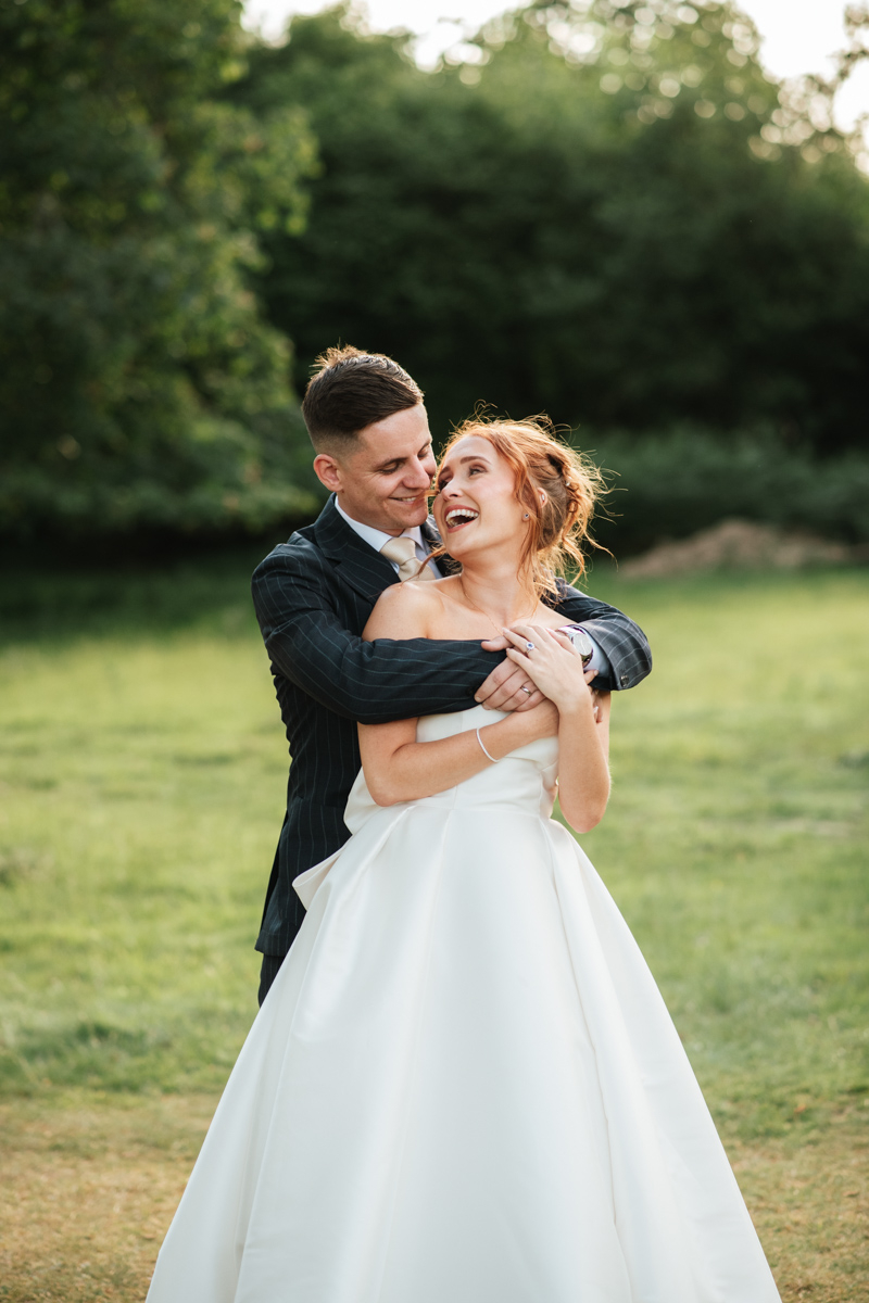 groom embracing his bride from behind as they laugh together at highley manor wedding venue 