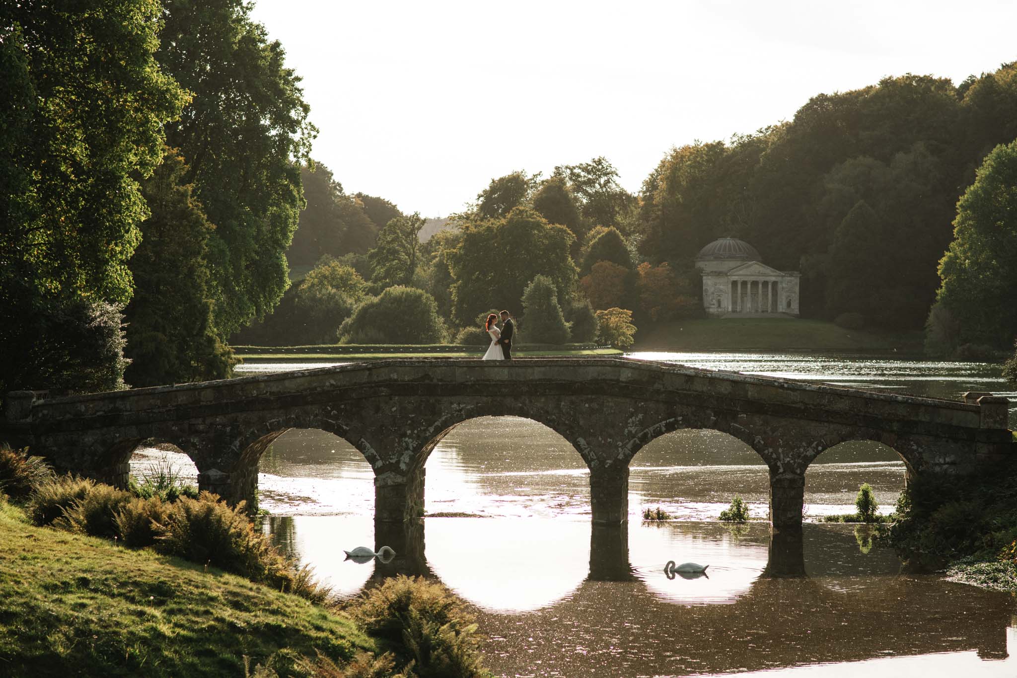 Bride and groom standing on the bridge over the rover at stourhead gardens in Wiltshire