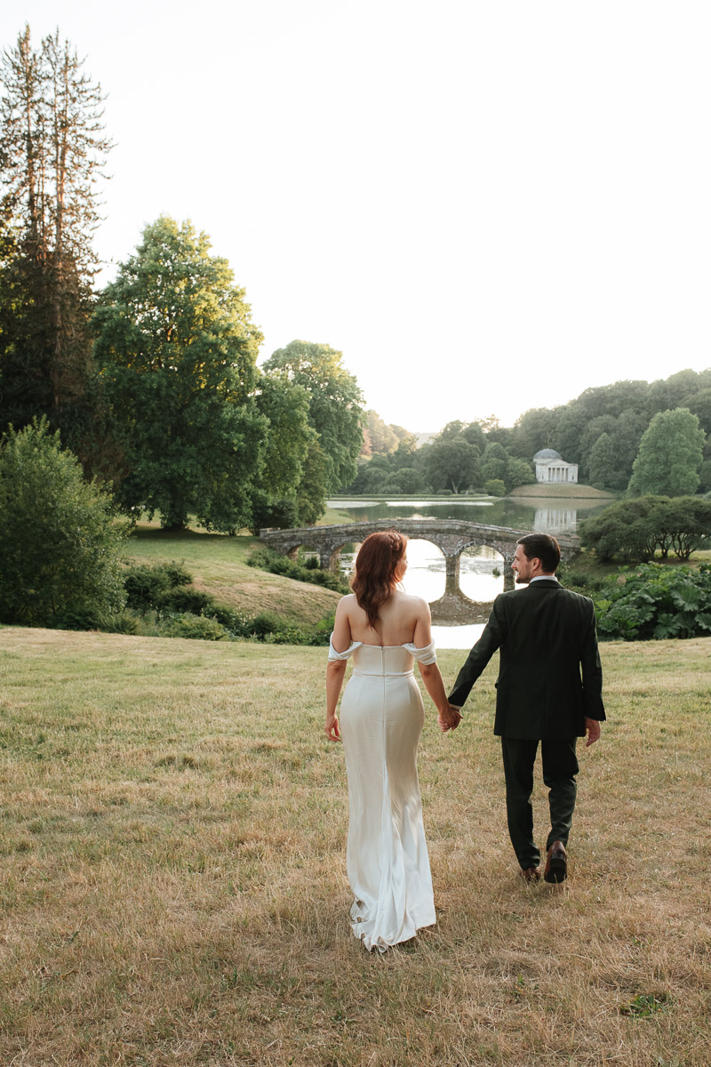 bride and groom walking hand in towards the bridge at stourhead gardens in Wiltshire 