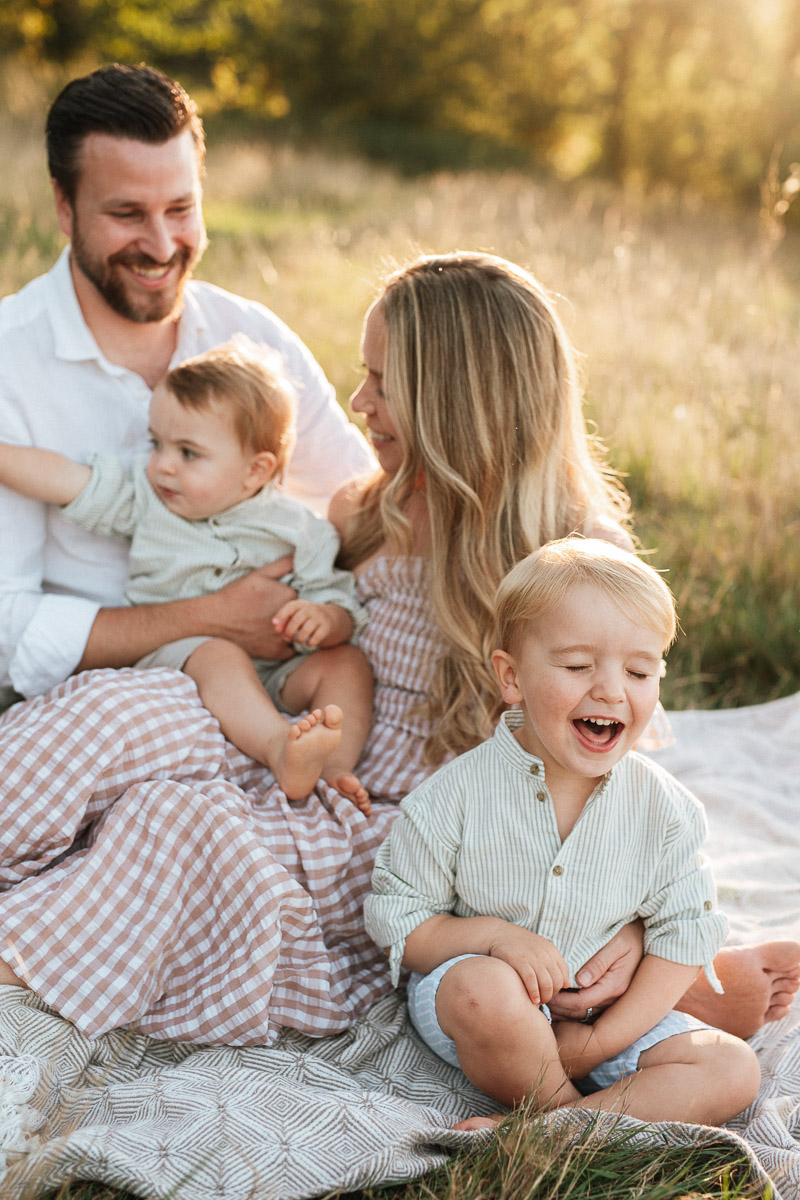 family of 4 sitting on a blanket during sunset