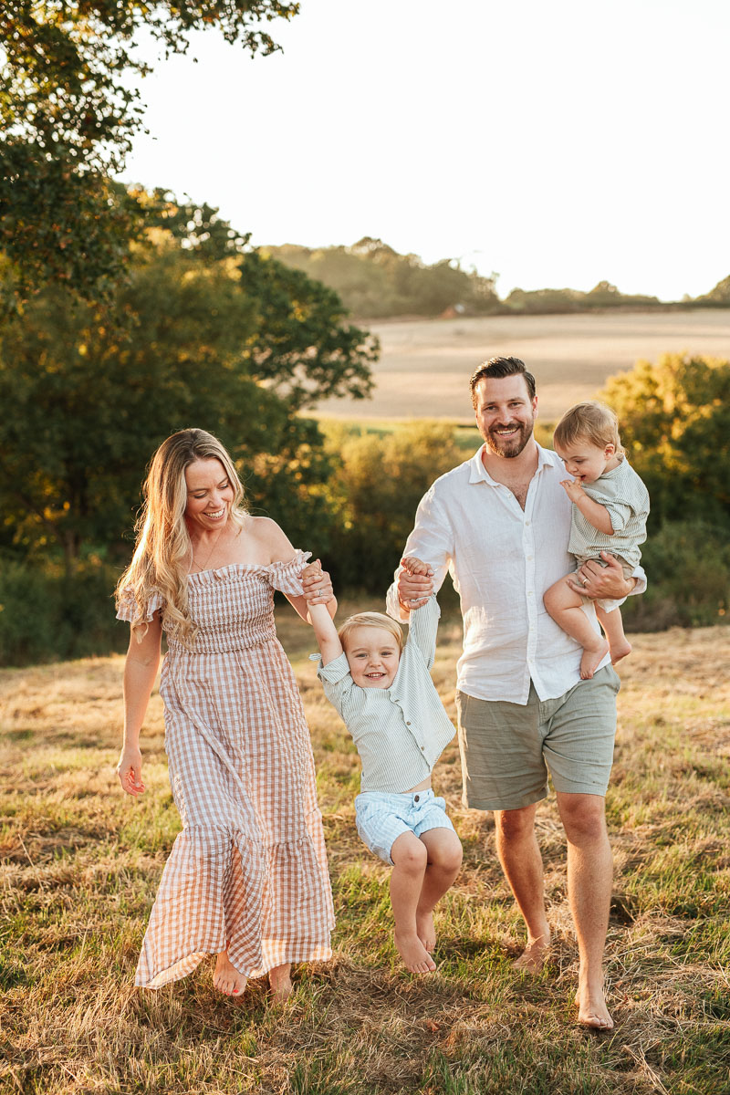 parents walking together with their two young children. They are swinging their boy in the air as they walk.
