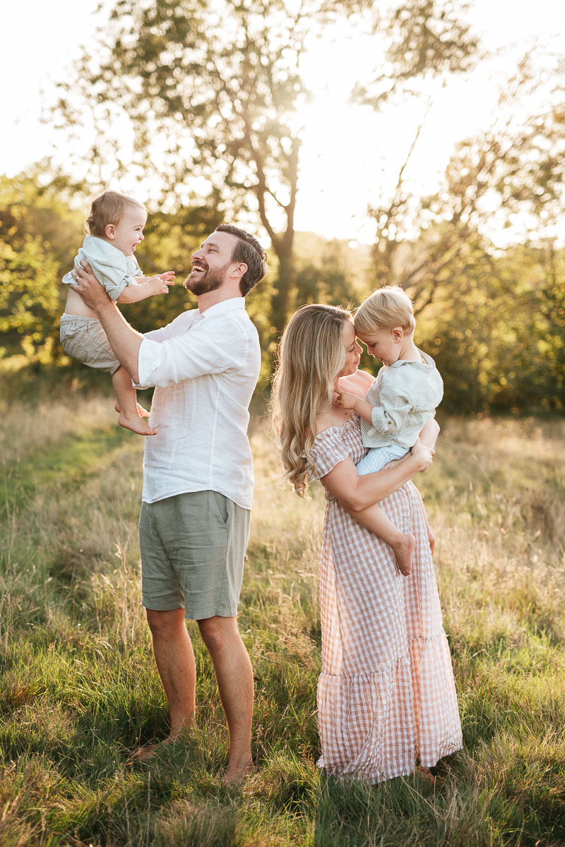 Parents standing back to back holding their children and cuddling them during family photography session with Wiltshire photographer Rachel Jane